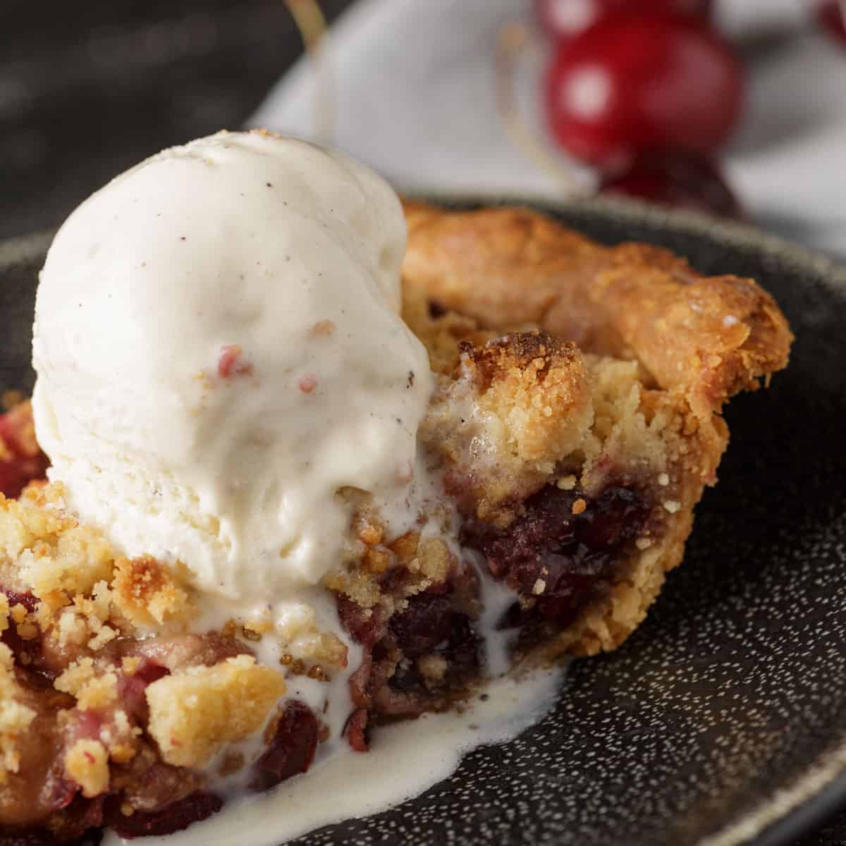 A slice of cherry pie with a scoop of ice cream.