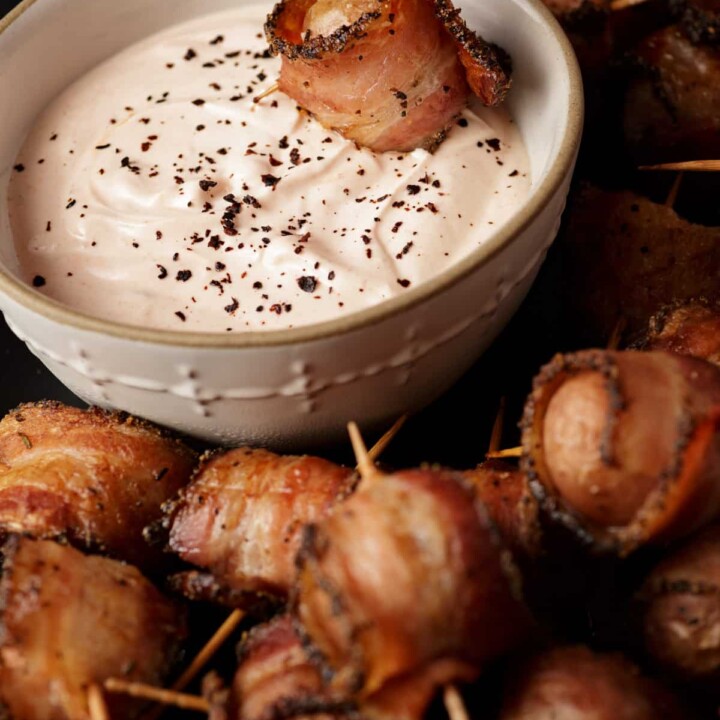 A bacon wrapped potato being dipped in sauce.