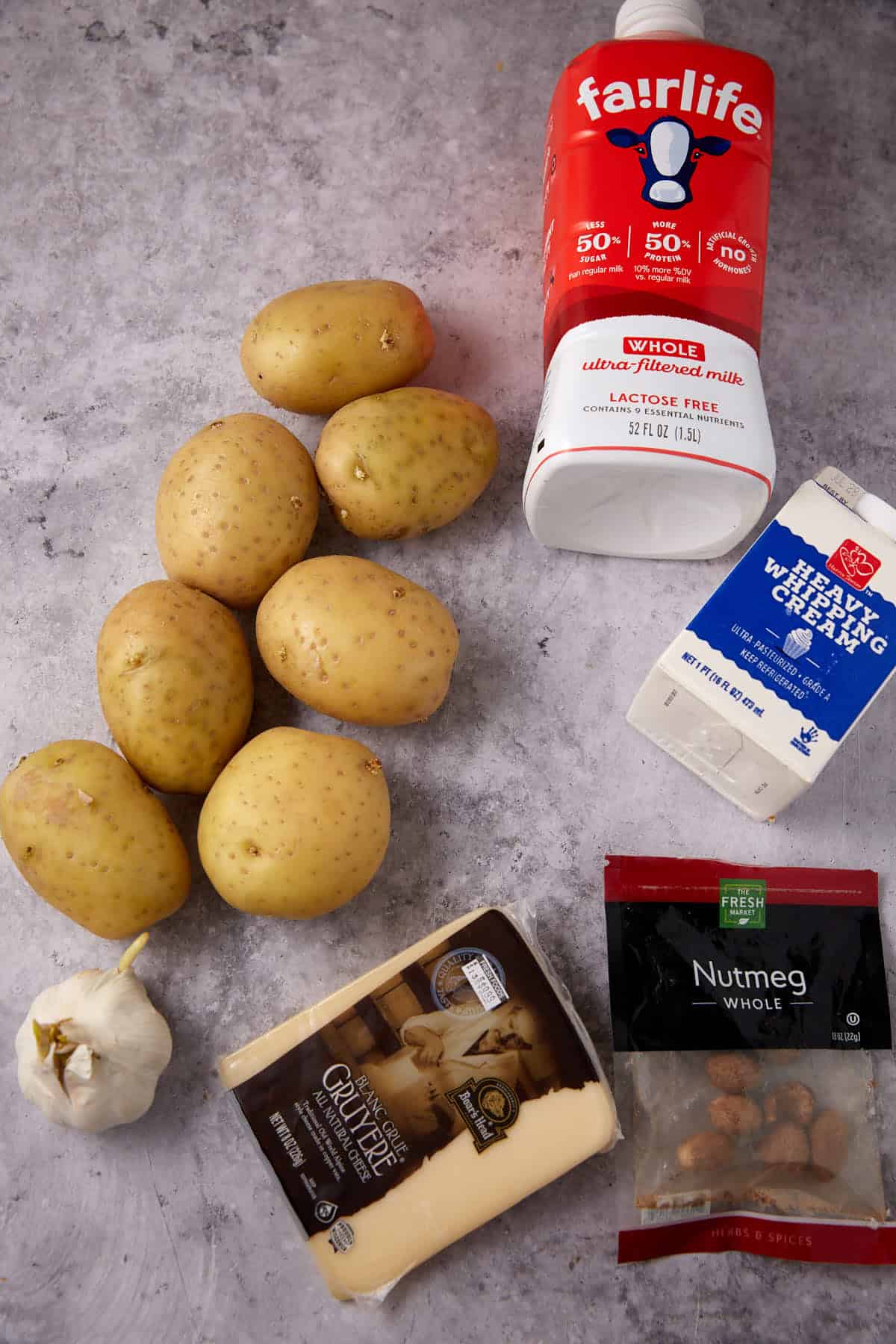 A lineup for perfect scalloped potatoes with cheese: Yukon Gold potatoes, garlic, Gruyère, lactose-free whole milk, heavy whipping cream cheese, and whole nutmeg—everything you need to make ahead scalloped potatoes with cream.