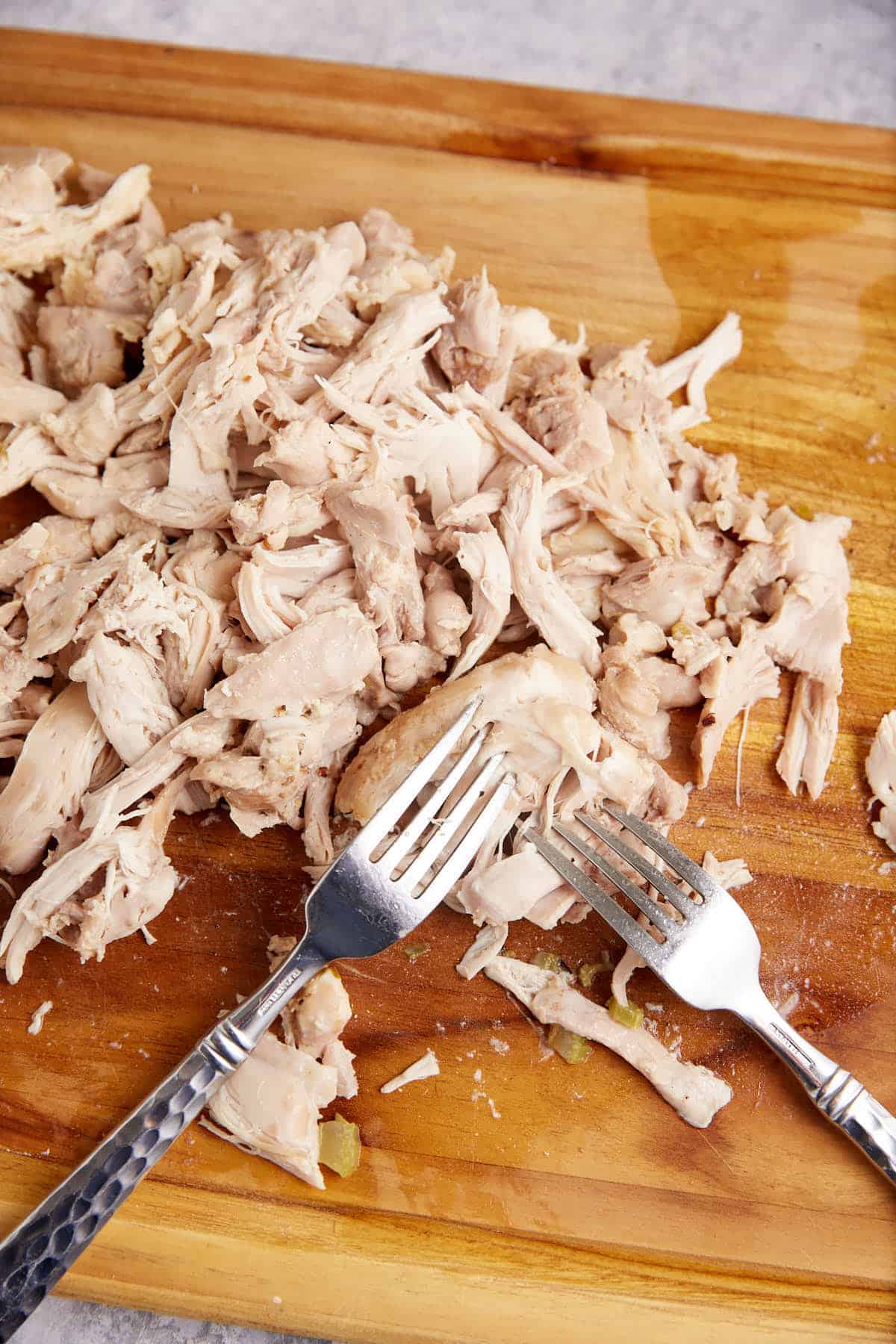 Chicken shredded with two forks on a cutting board.