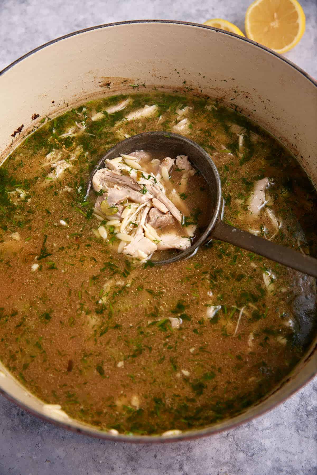 A pot of chicken orzo soup with a ladle.