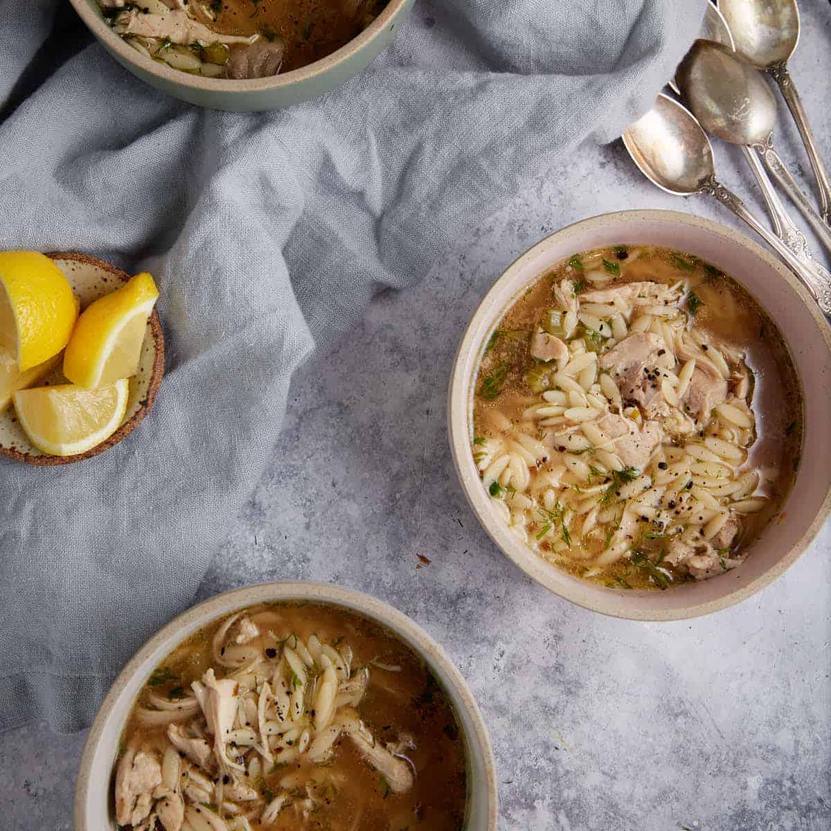 Three bowls of chicken orzo soup with lemon.