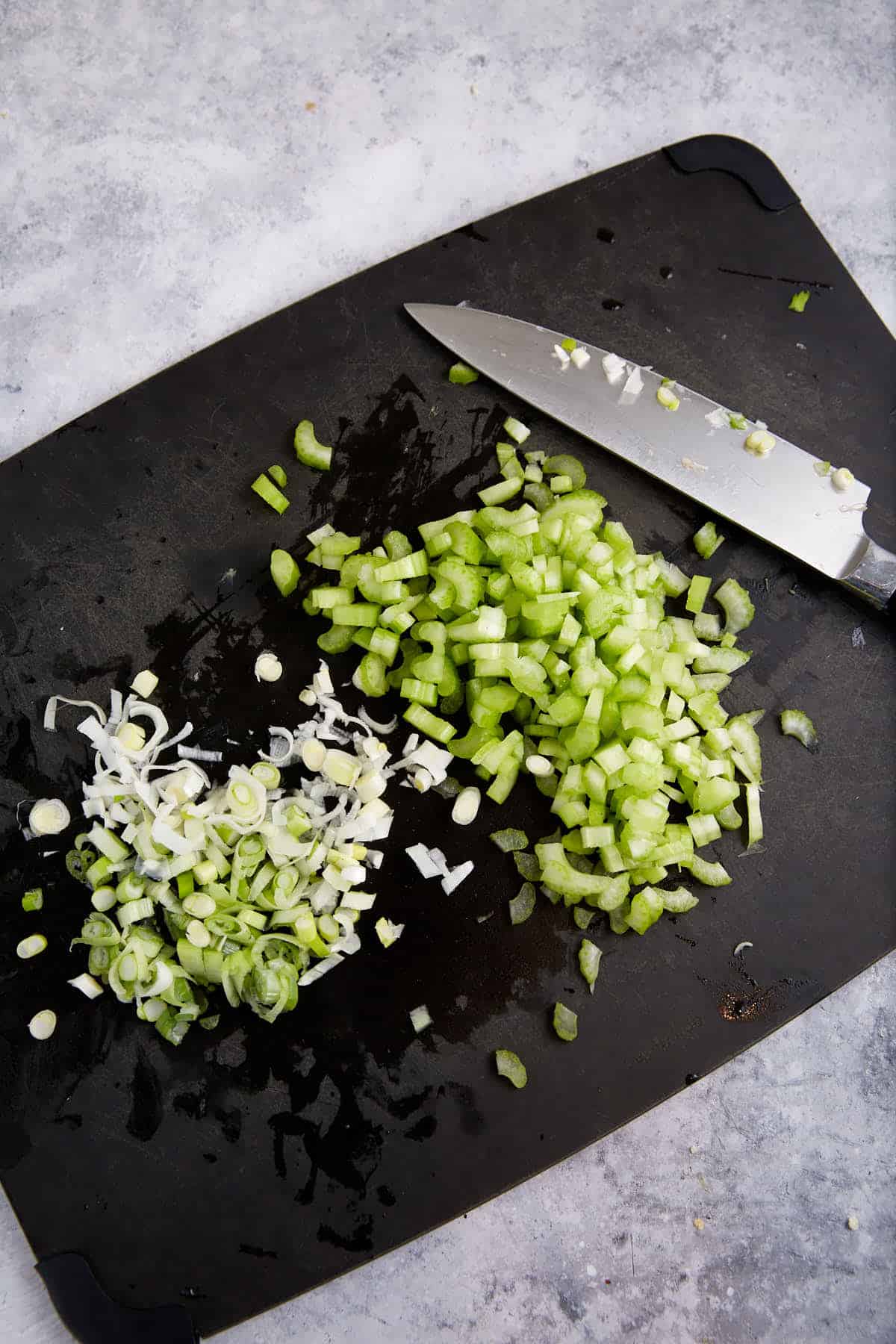 Celery and green onions chopped on a cutting board.