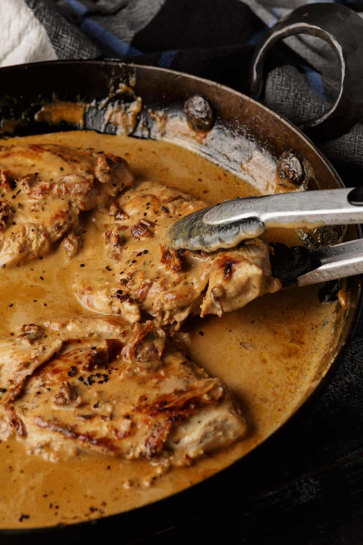 A chicken breast being removed from a skillet