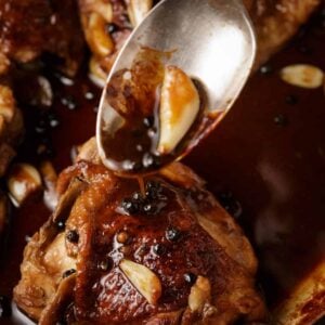 A spoon pouring sauce over a piece of chicken.