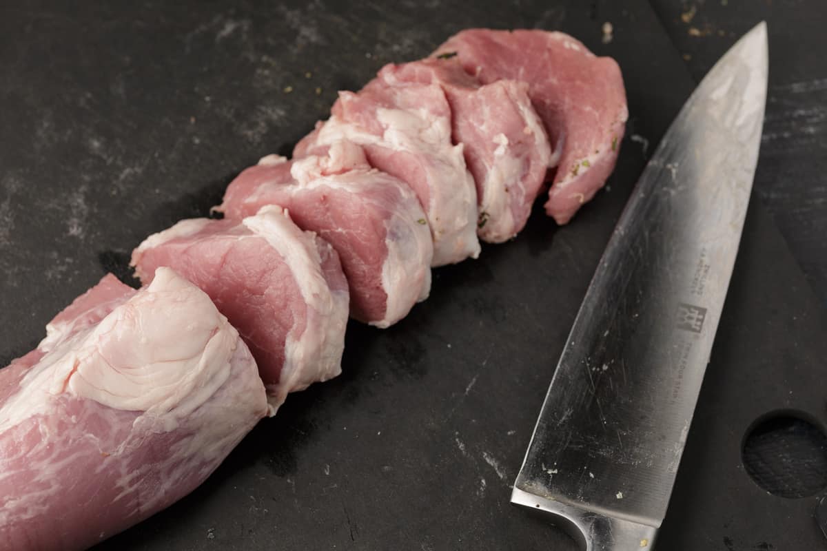 A pork tenderloin being sliced into medallions