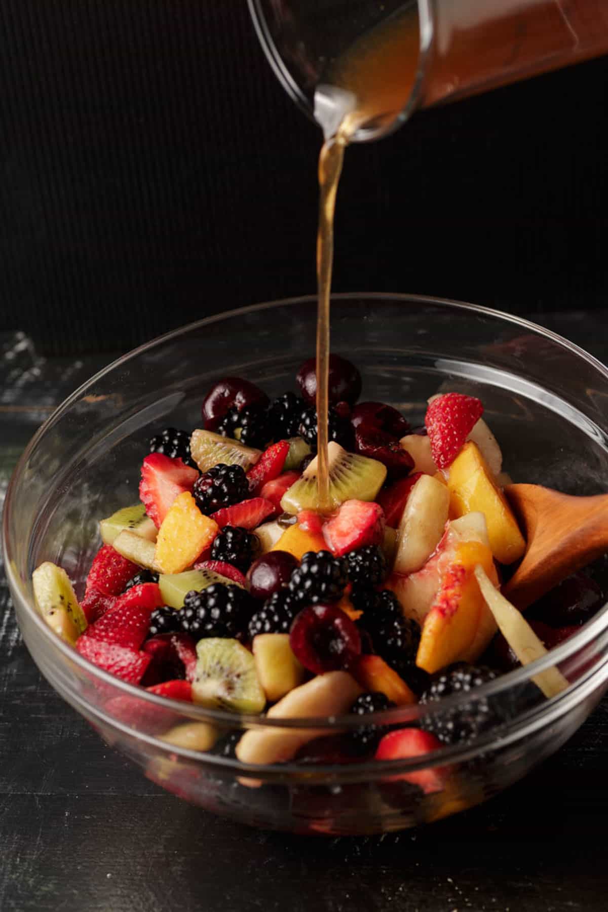 A bowl of summer fruit with dressing being poured over the top.