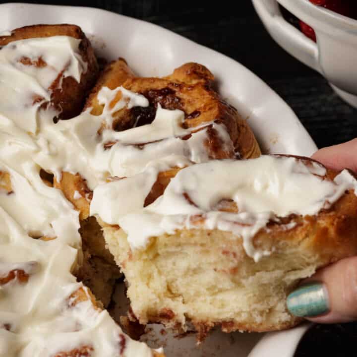 A cinnamon roll being pulled out of a baking dish.