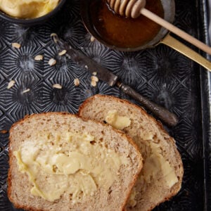 Two slices of oatmeal bread on a tray next to butter and honey.