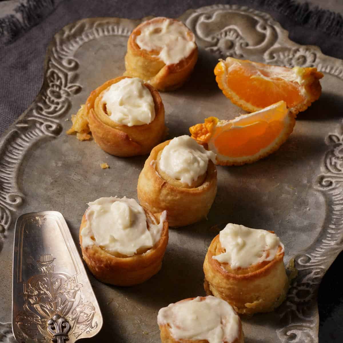 A silver tray with orange cinnamon rolls and some orange slices.