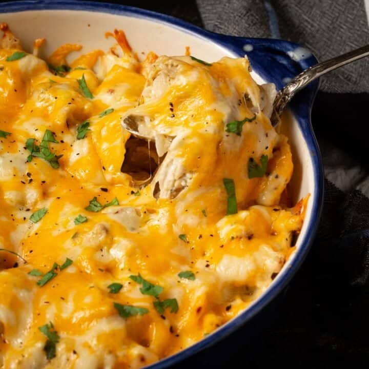 A spoon pulling the cheese up from a casserole dish of ranch chicken pasta.