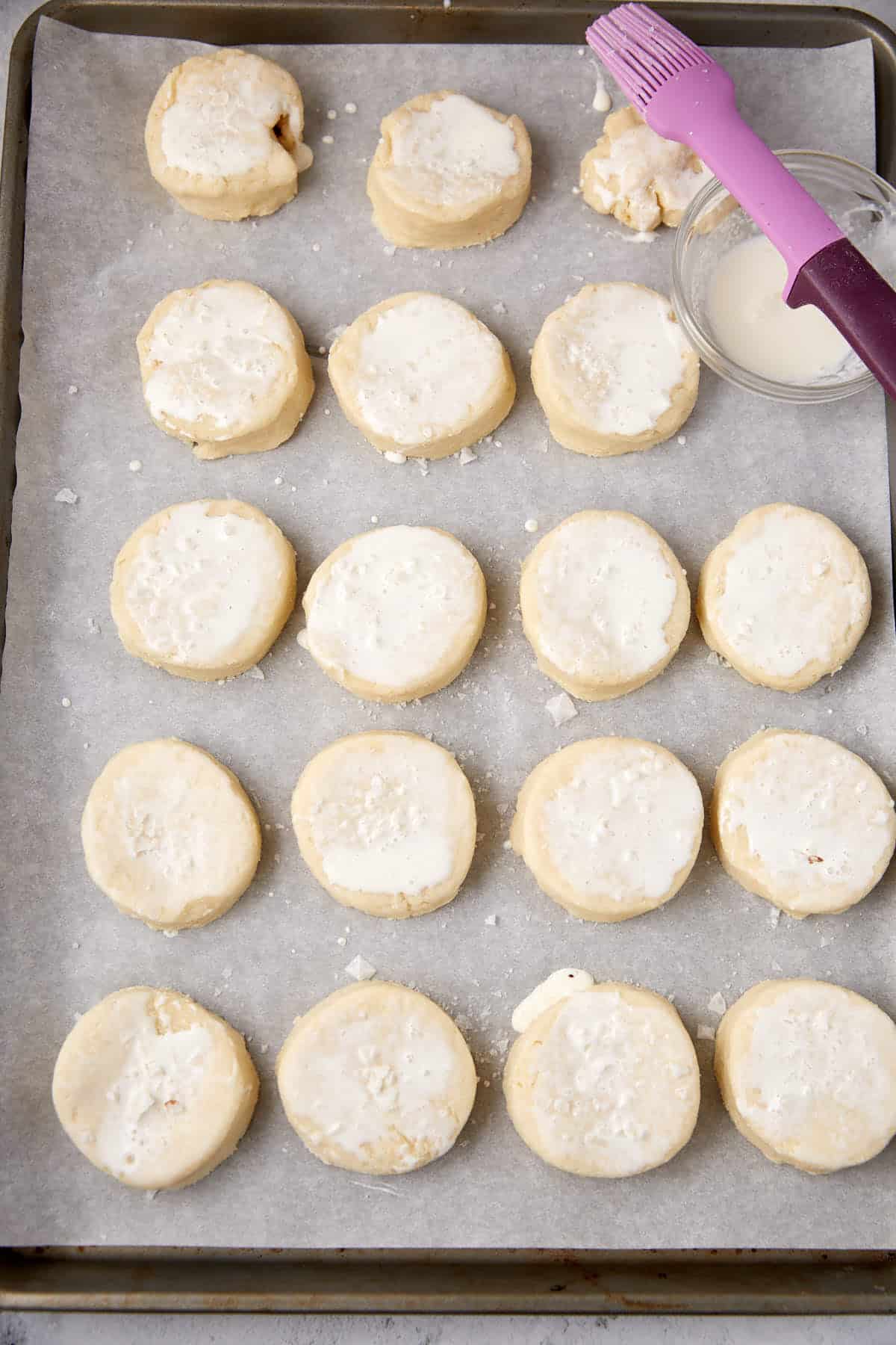 Biscuits brushed with cream on a baking tray.