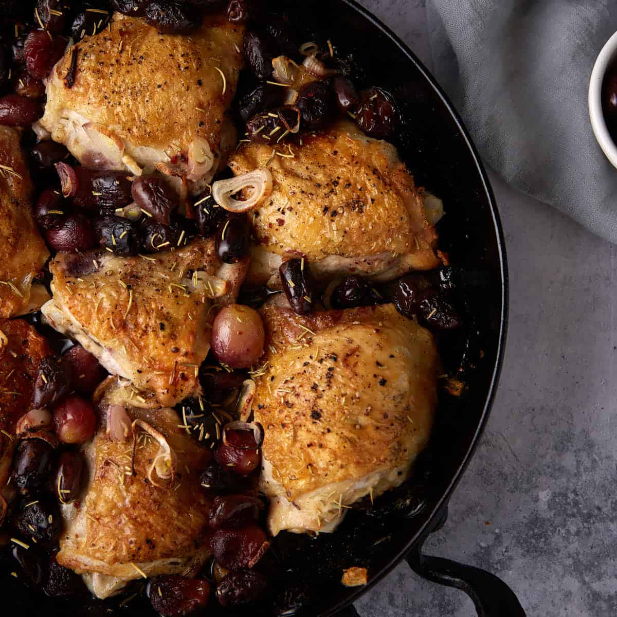 Grapes and olives with roasted chicken in a skillet.