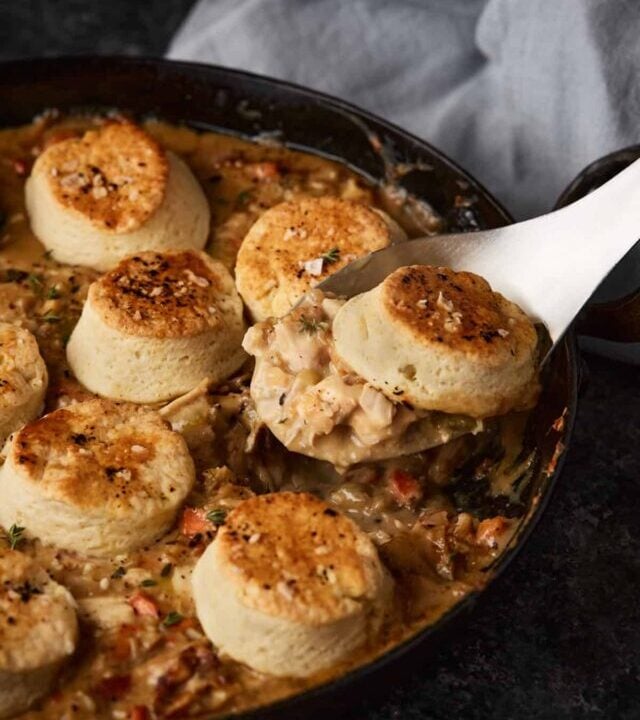 A serving spoon scooping out a biscuit with chicken pot pie.