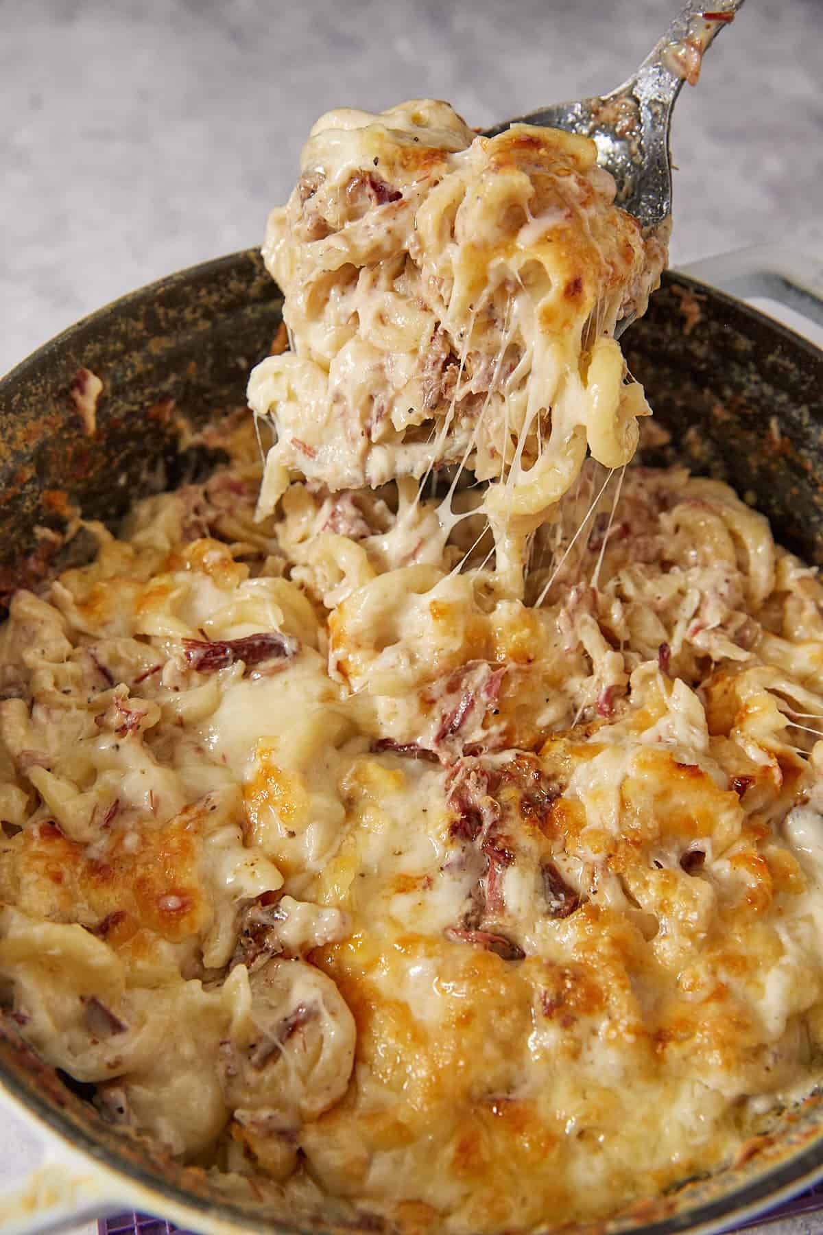 A close-up of a cheesy baked pasta dish being scooped from a pan, showing melted cheese stretching from the creamy, golden-brown pasta mixture—just like an old fashioned mac and cheese made from a classic southern baked macaroni and cheese recipe.