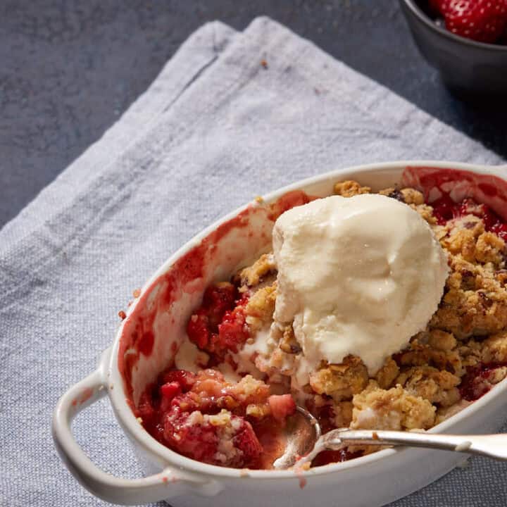 A ramekin of rhubarb and strawberry crumble with a scoop of ice cream.