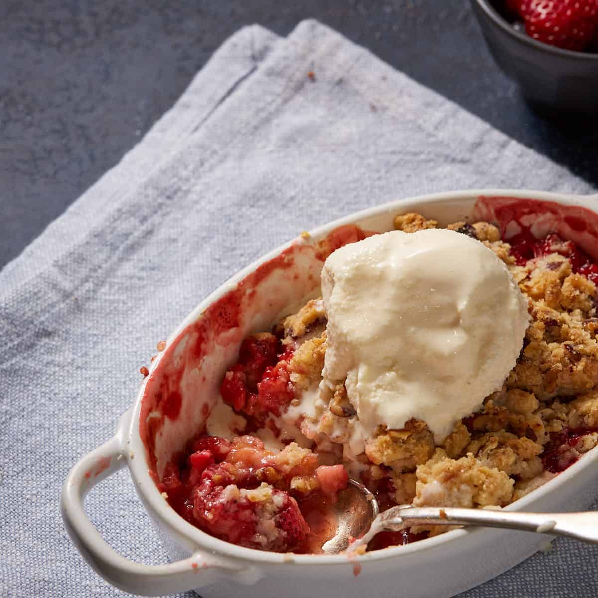 A ramekin of rhubarb and strawberry crumble with a scoop of ice cream.