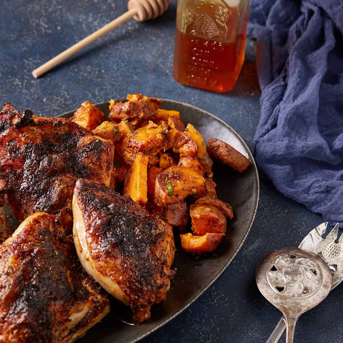 Chicken and sweet potatoes on a black platter next to serving spoons.
