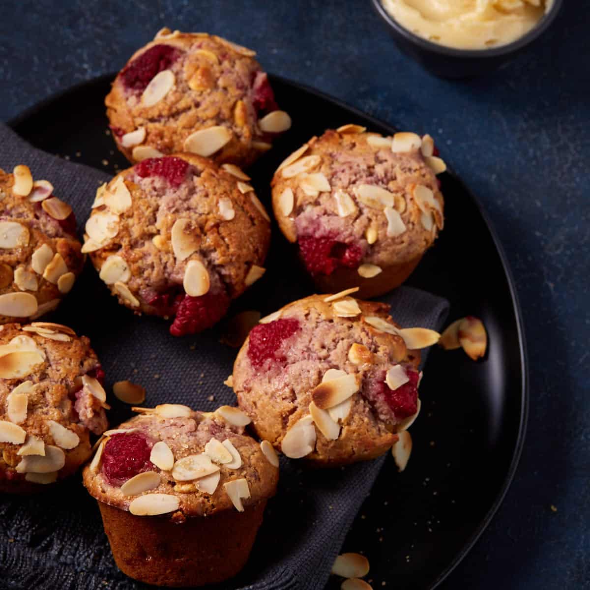 A platter of white chocolate muffins with raspberries.