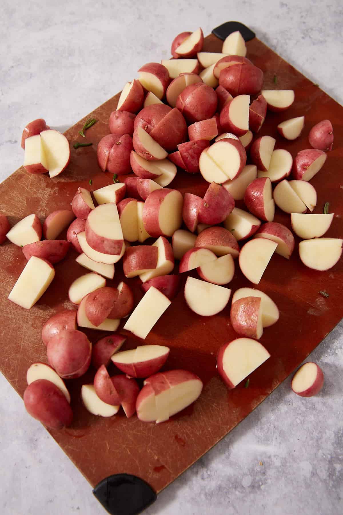 A pile of chopped red potatoes on a brown cutting board with black corner grips, set on a light-colored countertop—perfect for serving alongside baked lemon chicken or your favorite easy lemon chicken recipe.