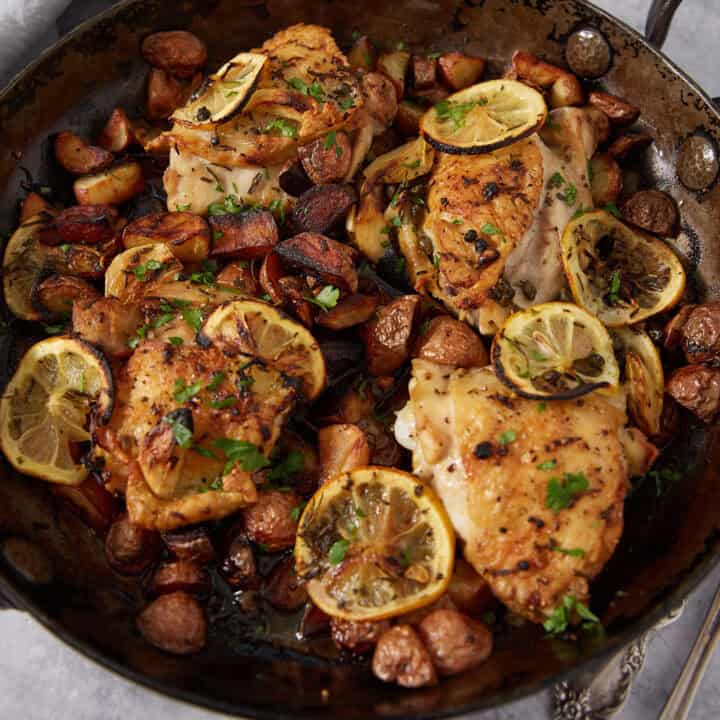 Baked lemon chicken thighs with sliced lemons and golden potatoes, garnished with chopped herbs and served in a rustic skillet—an easy lemon chicken recipe perfect for any cozy meal.