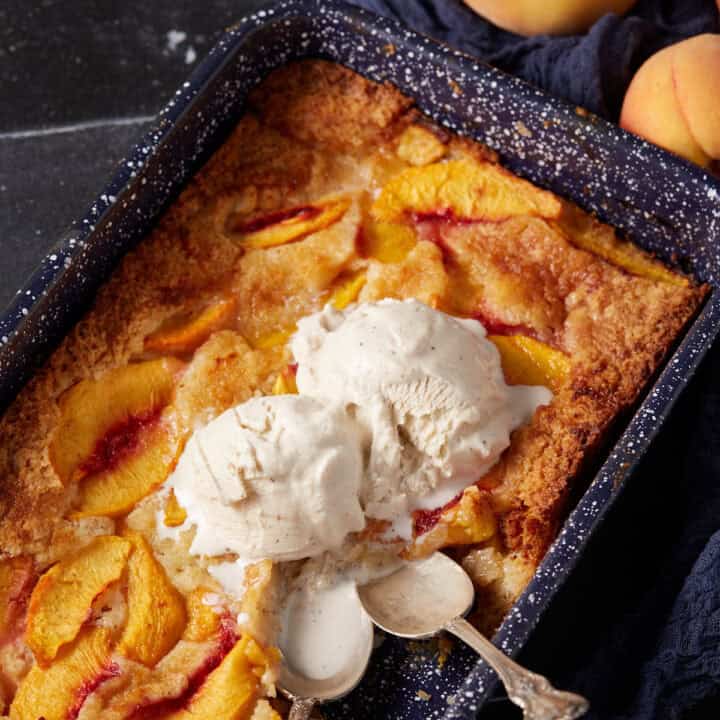 Two scoops of vanilla ice cream over a peach cobbler cake.