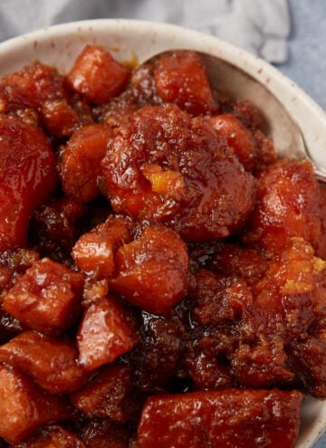 A bowl filled with southern candied yams, coated in a thick, caramelized brown sugar sauce, with a silver spoon resting on the side.