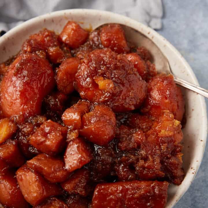 A bowl filled with southern candied yams, coated in a thick, caramelized brown sugar sauce, with a silver spoon resting on the side.