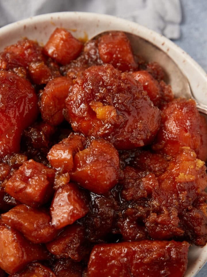 A bowl filled with southern candied yams, coated in a thick, caramelized brown sugar sauce, with a silver spoon resting on the side.