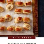 A baking sheet covered with parchment paper holds numerous golden brown, bite-sized Puff Pastry Sausage Rolls, perfectly spaced.