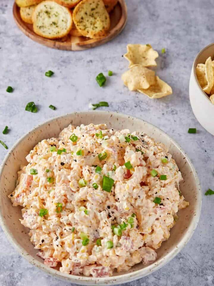 Corn dip in a bowl next to chips and crackers.
