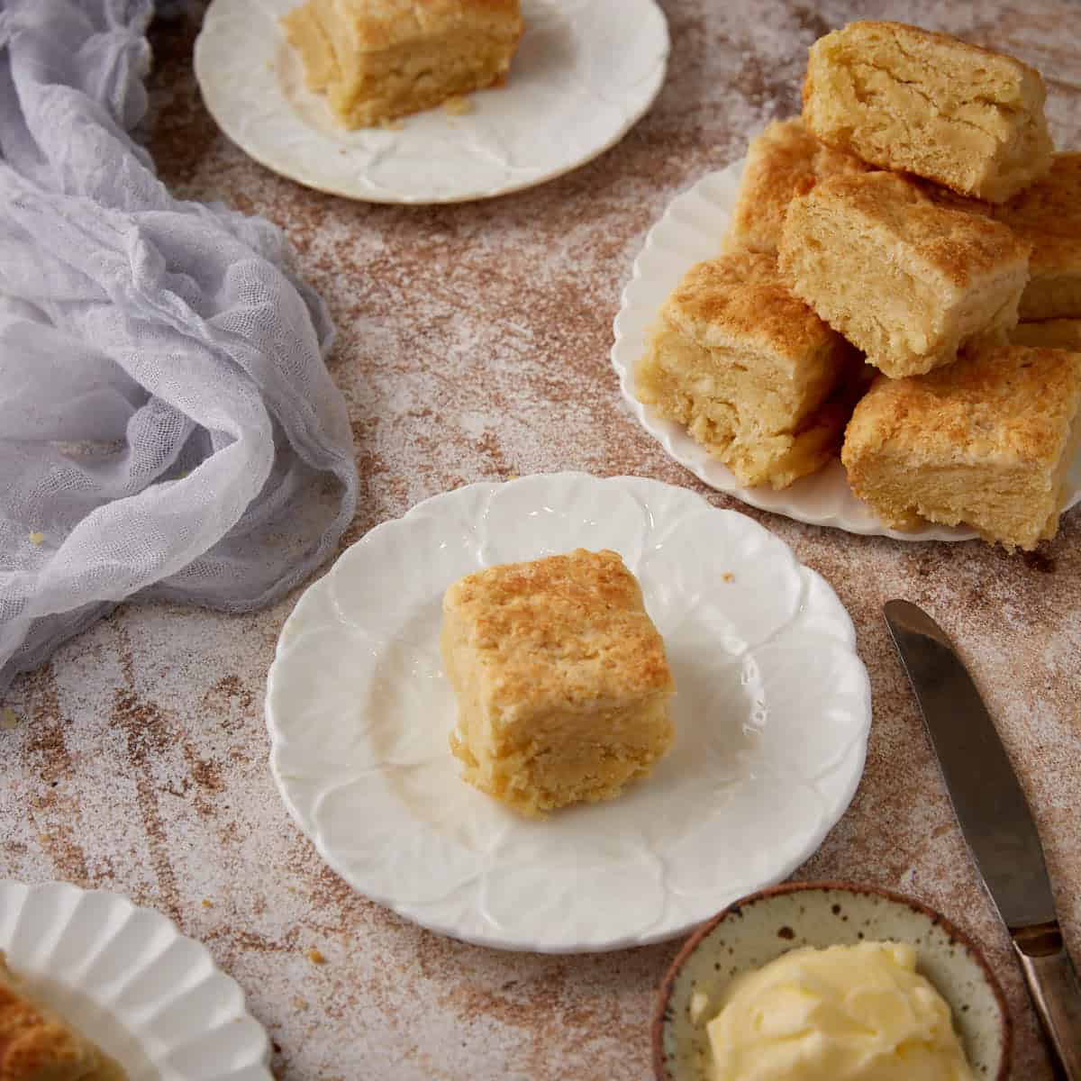 A single butter biscuit next to a platter of biscuits.