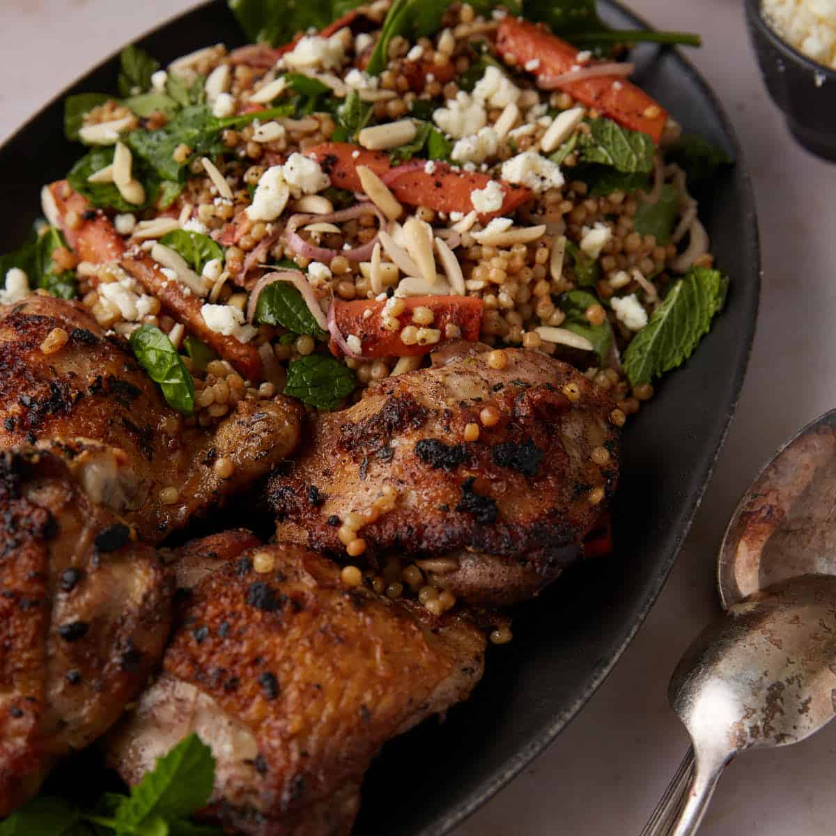A platter of chicken thighs next to couscous.