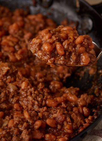 A serving spoon of baked beans with hamburger.