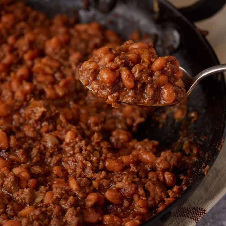 A serving spoon of baked beans with hamburger.