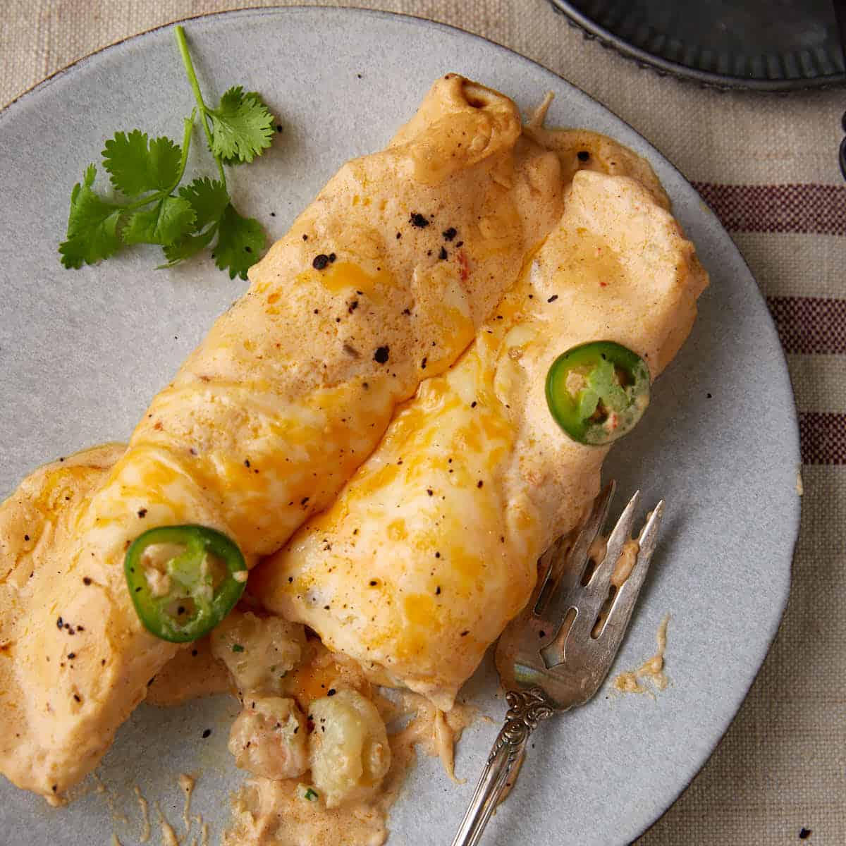 Shrimp enchiladas on a plate with jalapeno slices on top.
