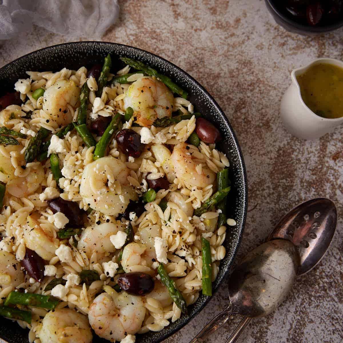 A serving bowl of shrimp pasta with kalamata olives.