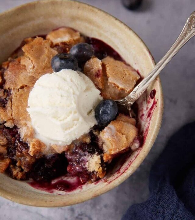 A bowl of blueberry self-saucing pudding with a spoon.