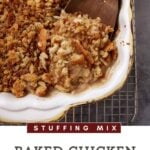 A close-up of a baked chicken casserole in a rectangular white dish. The casserole is topped with a golden, crispy layer of chicken stuffing. A wooden spoon scoops out a portion, revealing its creamy texture underneath.