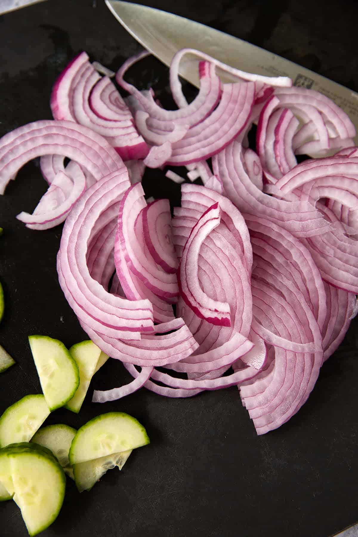 Cucumbers and onions sliced on a cutting board.