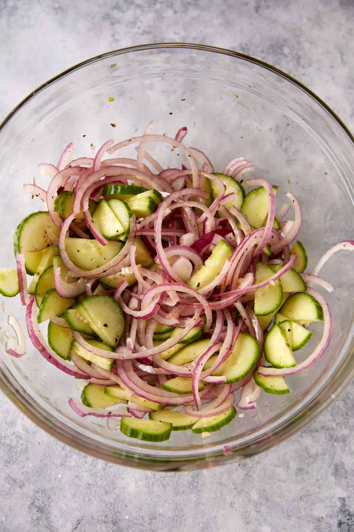 Cucumbers and onions marinating in a glass bowl.