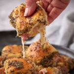 A Hawaiian roll slider being lifted from a platter.