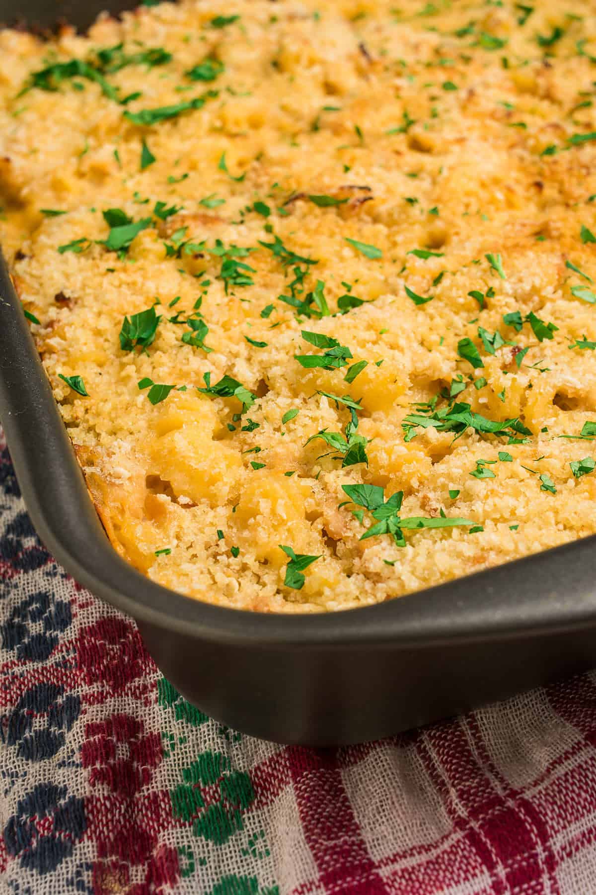 A close-up of baked macaroni and cheese in a rectangular pan, topped with golden breadcrumbs and chopped parsley, sits on a patterned cloth—sharing comfort food appeal with classic chicken noodle casserole.