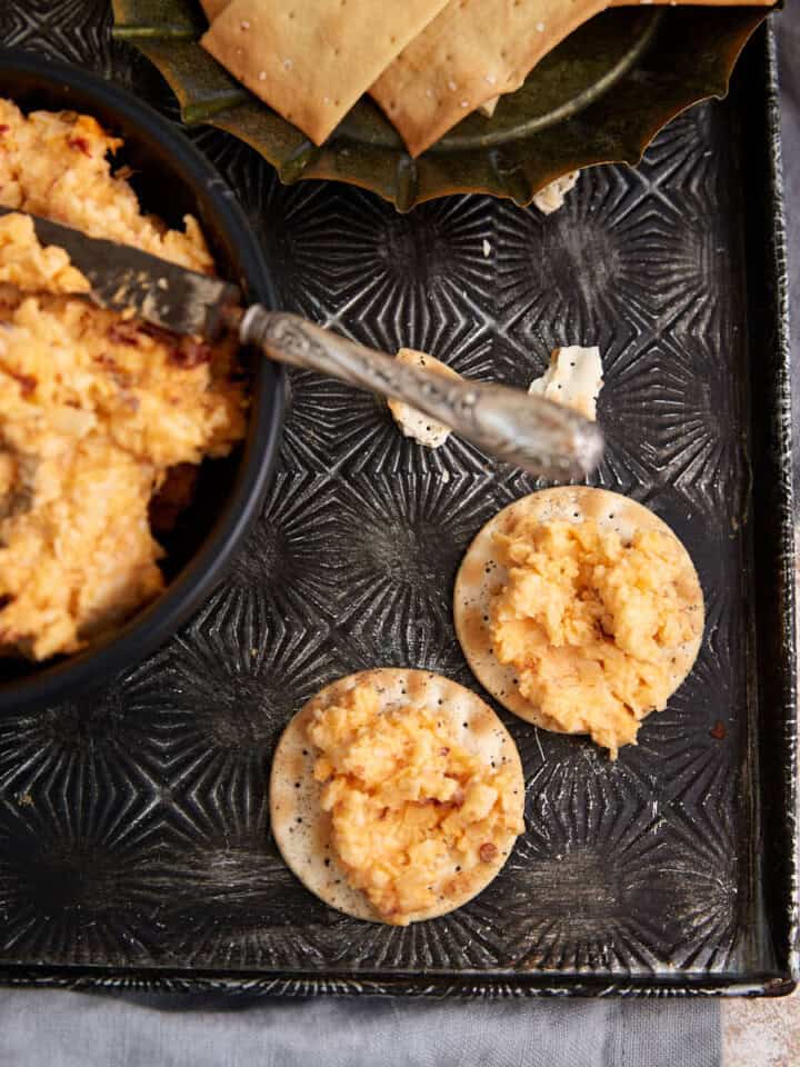 Two crackers with pimento cheese next to a bowl of cheese dip.