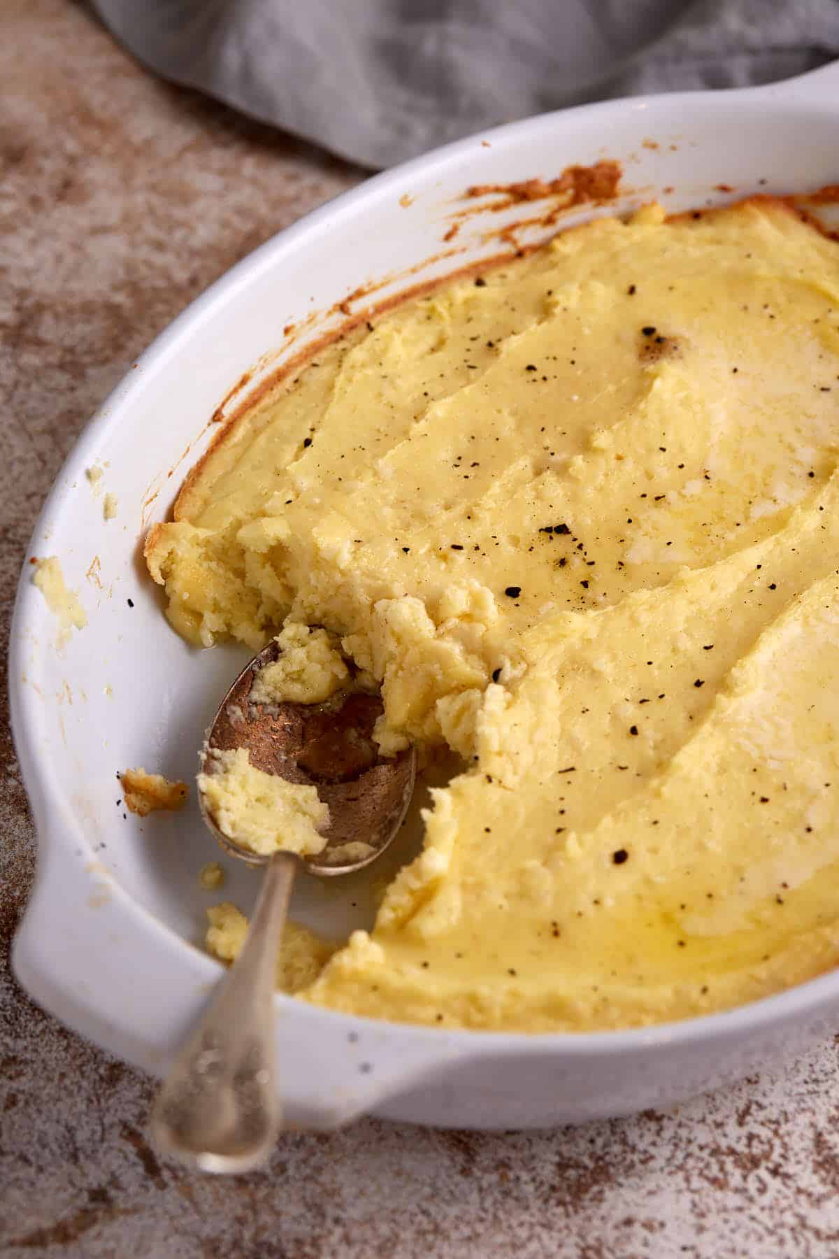 A spoon bread in a baking dish with a serving spoon.