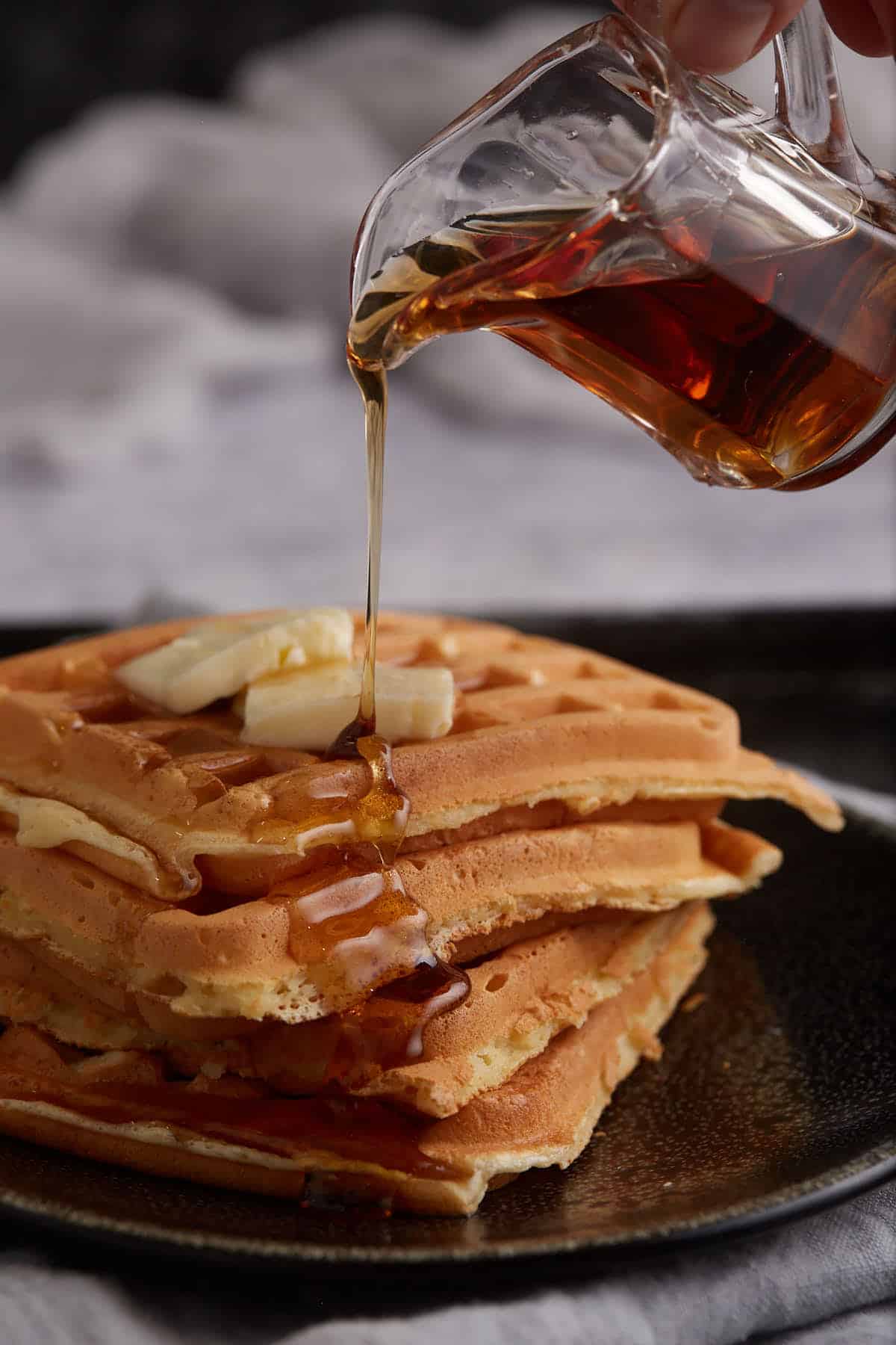 A plate of waffles with syrup being poured on top.