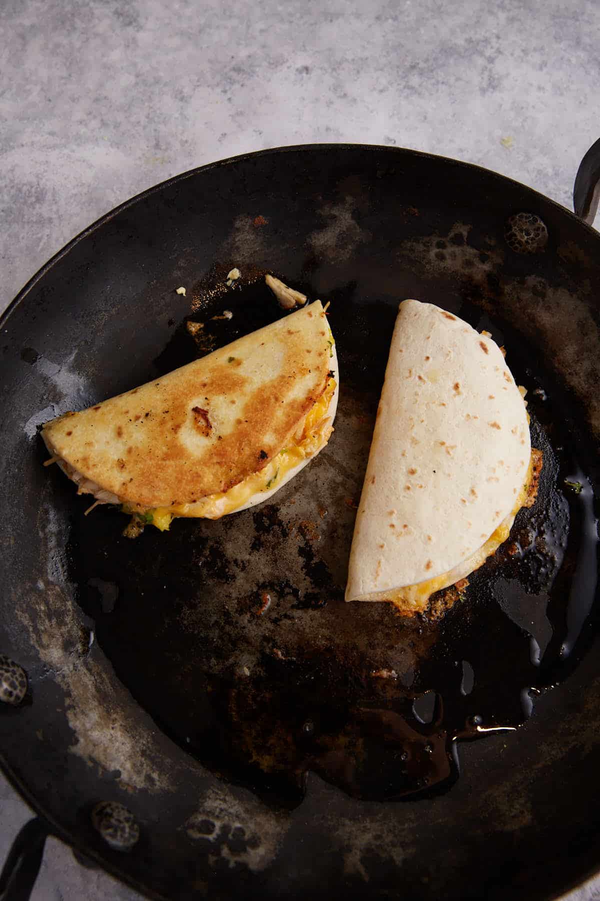 Two quesadillas cooking in a skillet.