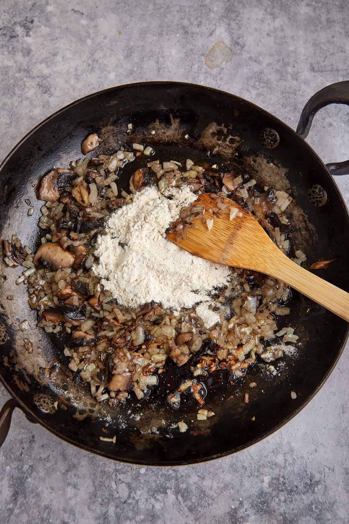 Cooked mushrooms and onions with flour on top in a skillet.