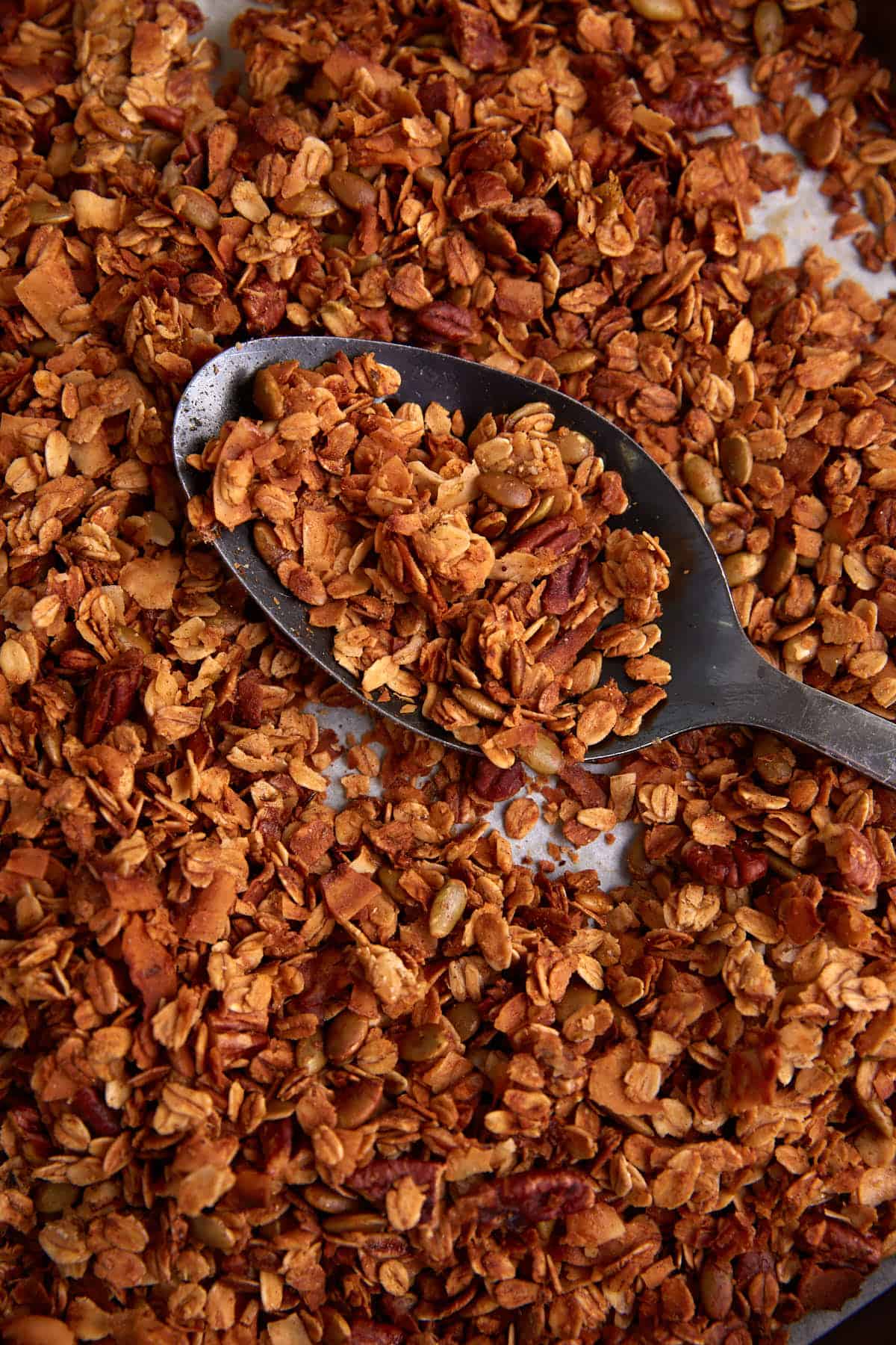 A spoon scooping up granola from a baking sheet.
