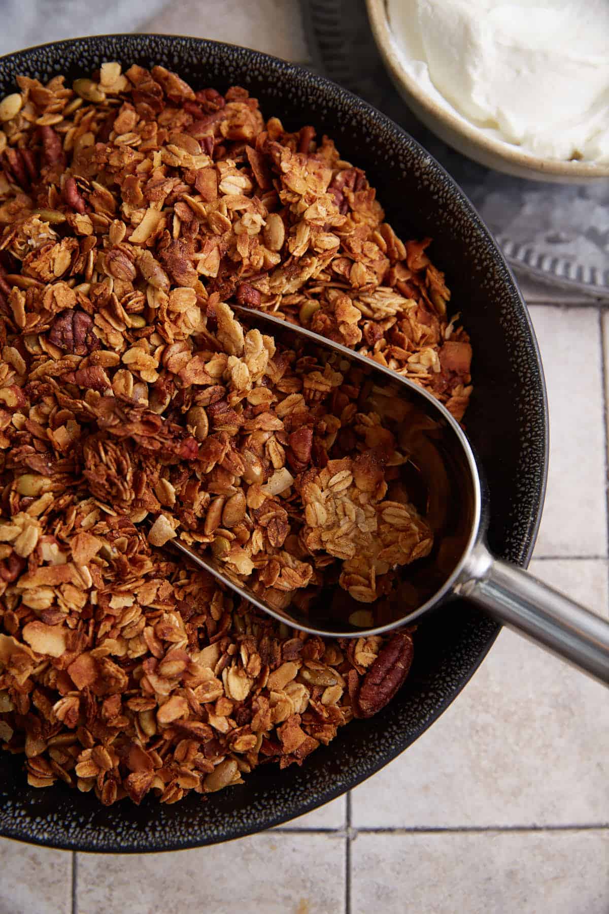 A scoop of granola next to a bowl of yogurt.